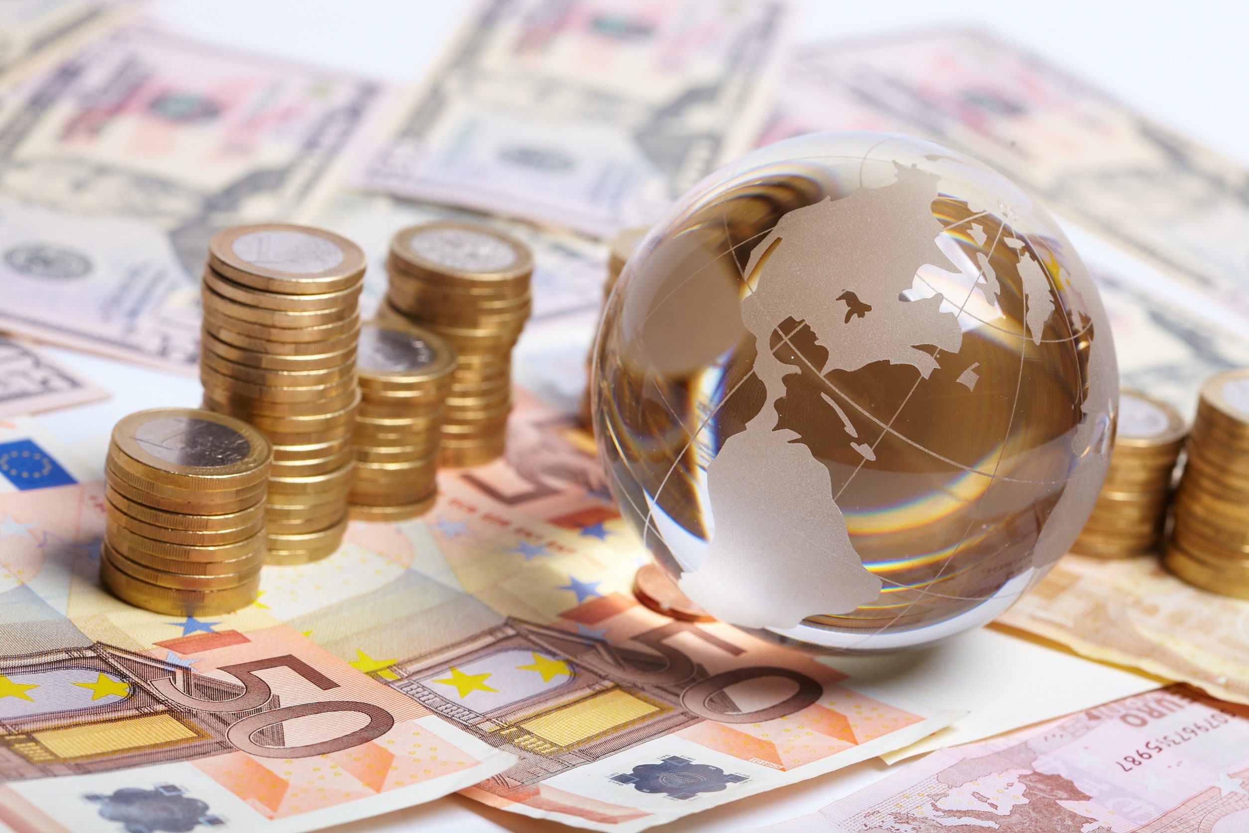 Glass globe on euro banknotes, next to piles of coins