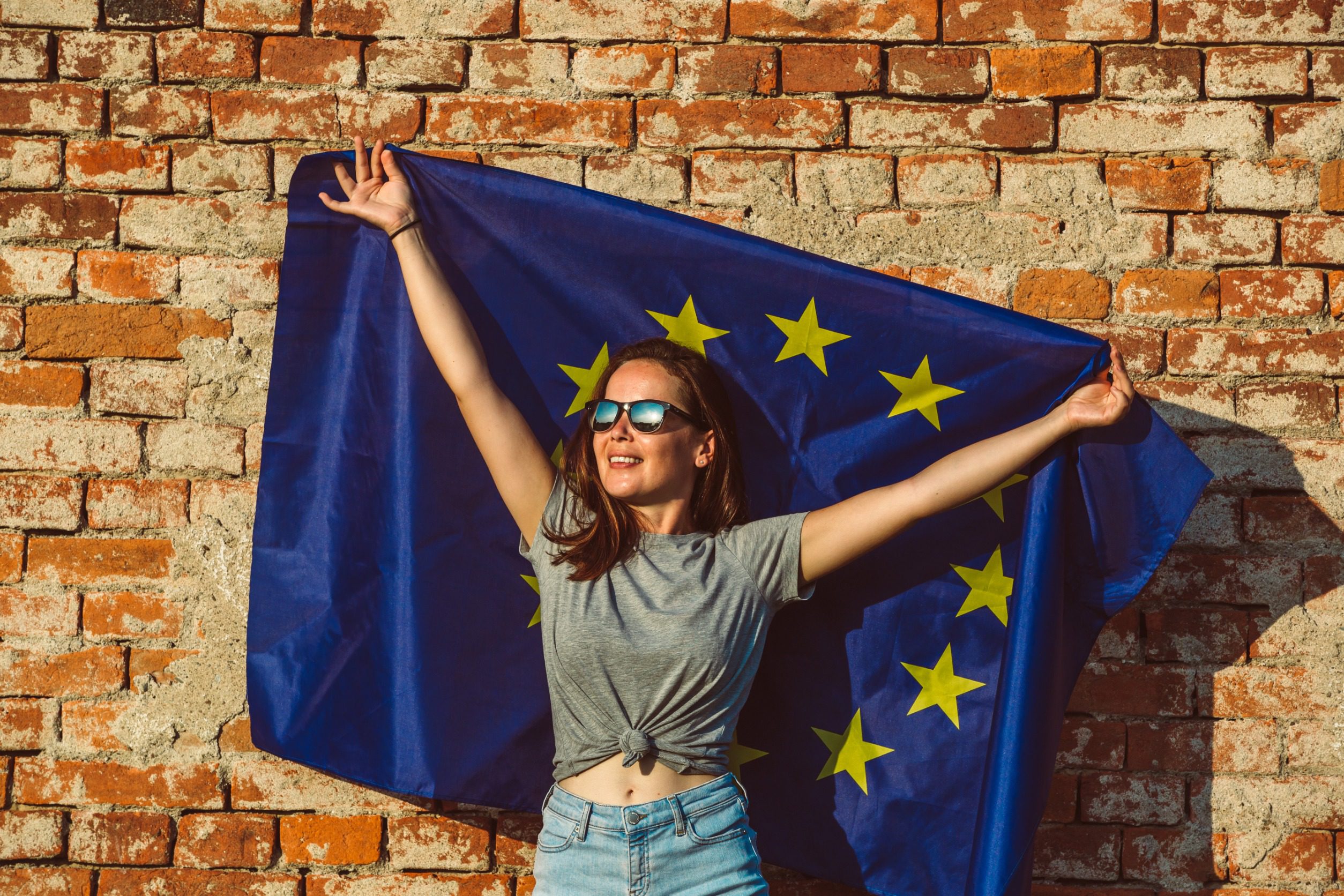 Młoda szczęśliwa kobieta trzymająca flagę Unii Europejskiej promującą koncepcję polityki UE