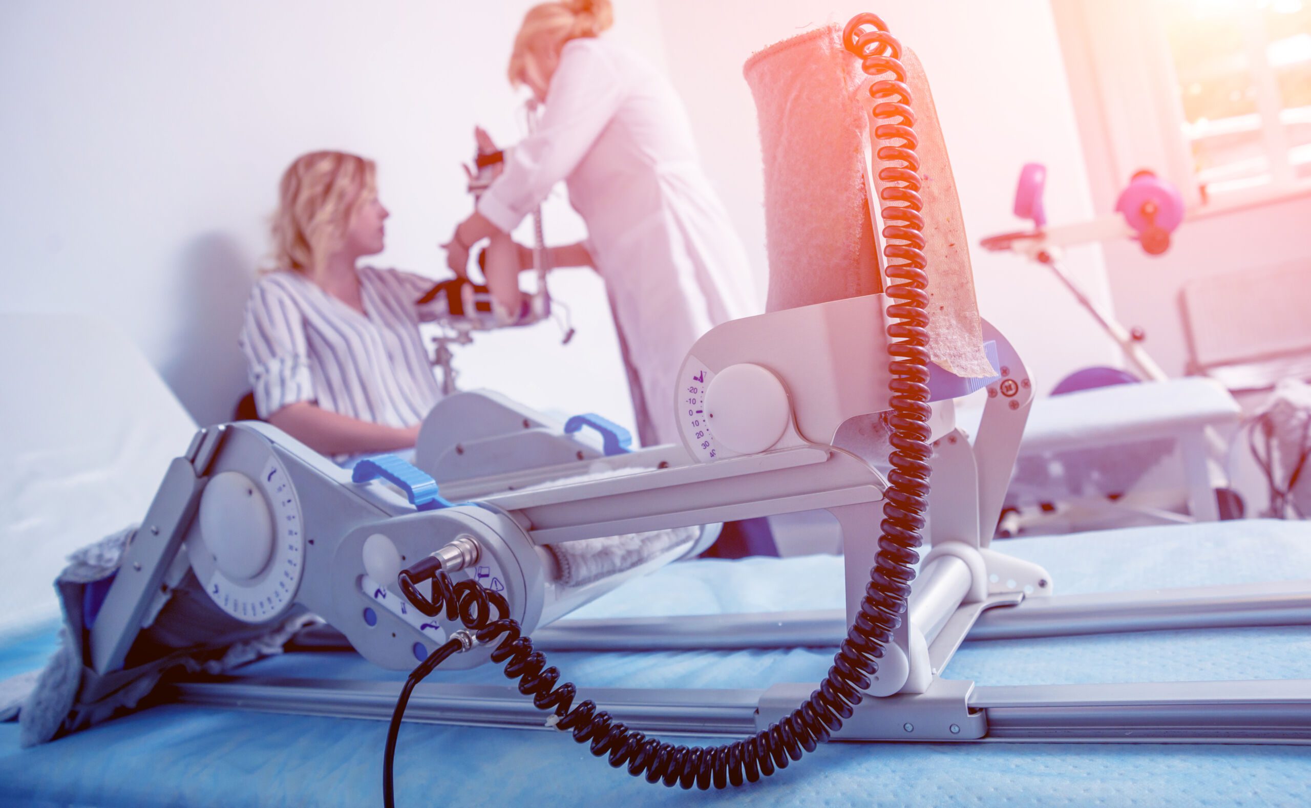 Zdjęcie ma charakter promocyjny. Przedstawia lekarza rehabilitującego pacjenta przy użyciu nowoczesnego sprzętu medycznego